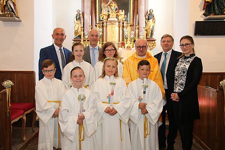 Gruppenfoto der Erstkommunikanten: Nina Danzinger, Emma Holzmüller und Linus Hipp, mit Pater Daniel, Bürgermeister Schaden, Vizebürgermeister Günter Prinz, Direktor Bernhard Bachofner und Klassenlehrerin Kerstin Kolm, sowie den Ministranten Bernhard Krecek, Lena und Julia Poppinger.